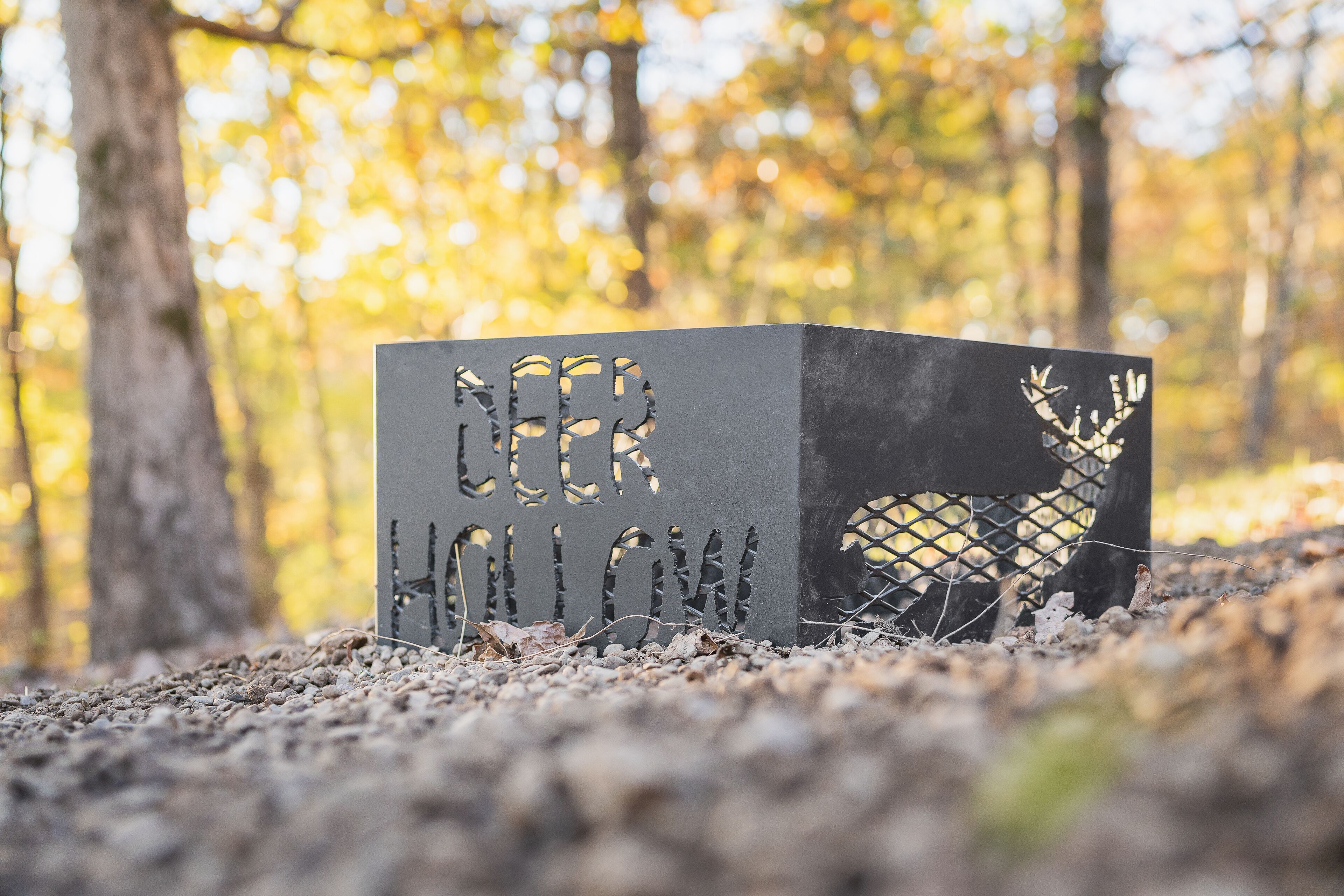 Un panneau en métal en forme de cerf, sur lequel on peut lire le texte « Deer Hollow », est posé sur le sol d’une forêt.