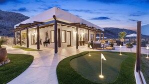 A modern house with a covered patio, a well-maintained lawn, and a golf putting area.