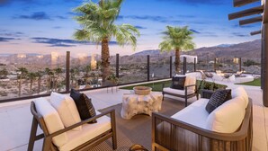 A terrace with outdoor seating, palm trees, and a view of a desert landscape.
