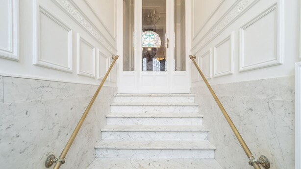 A marble staircase with gold handrails leading to a door with a stained glass window.