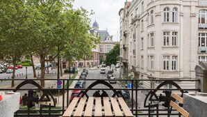 A view from a balcony overlooking a street with parked cars and buildings.