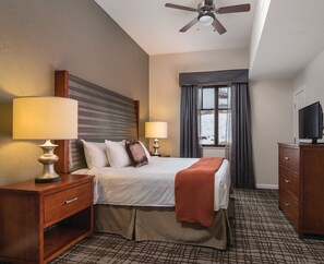 Relax in a cozy space with a comfortable bed, bedside lamps, and a TV on a wooden cabinet, offering a view of the outdoors.