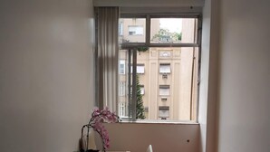 A room with a window, a white table, a chair, and a potted orchid. - Apartamento no Coração de Copacabana (Rio de Janeiro)