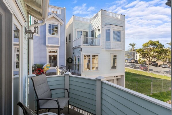 A balcony with a chair, overlooking a residential area with houses and parked cars.