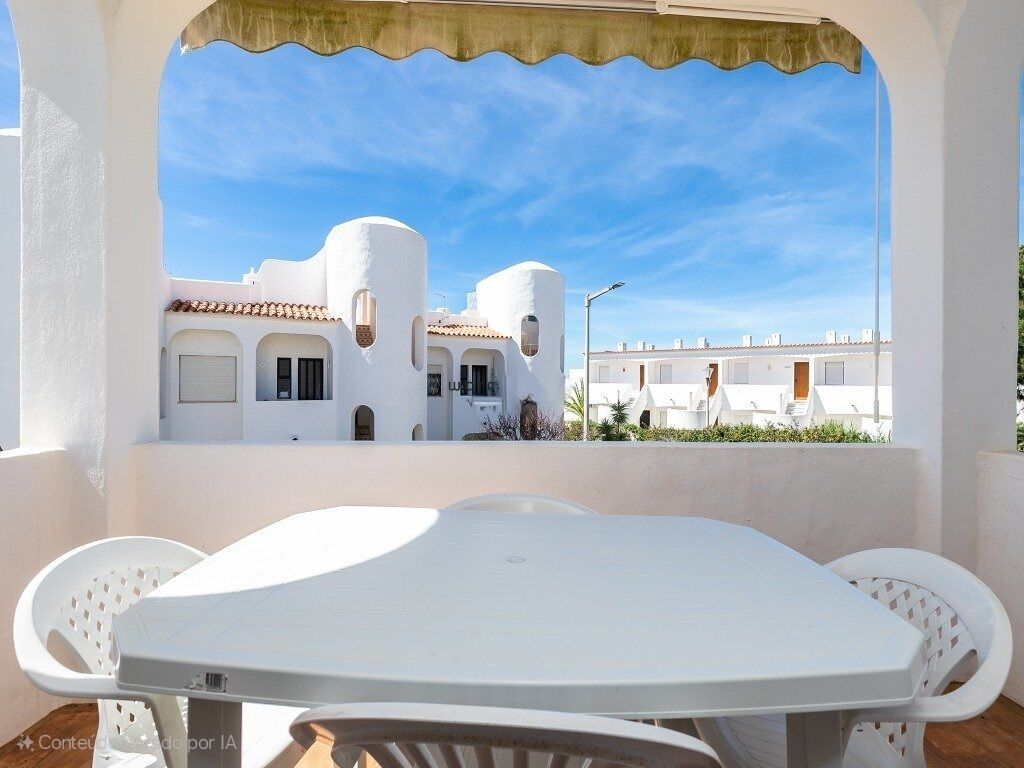 Une terrasse extérieure blanche, avec une table et des chaises, donnant sur un bâtiment blanc doté d’un toit en tuiles de terre cuite et de fenêtres en arc de cercle.