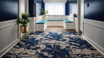 Un pasillo con alfombra azul estampada, un banco y plantas en macetas.