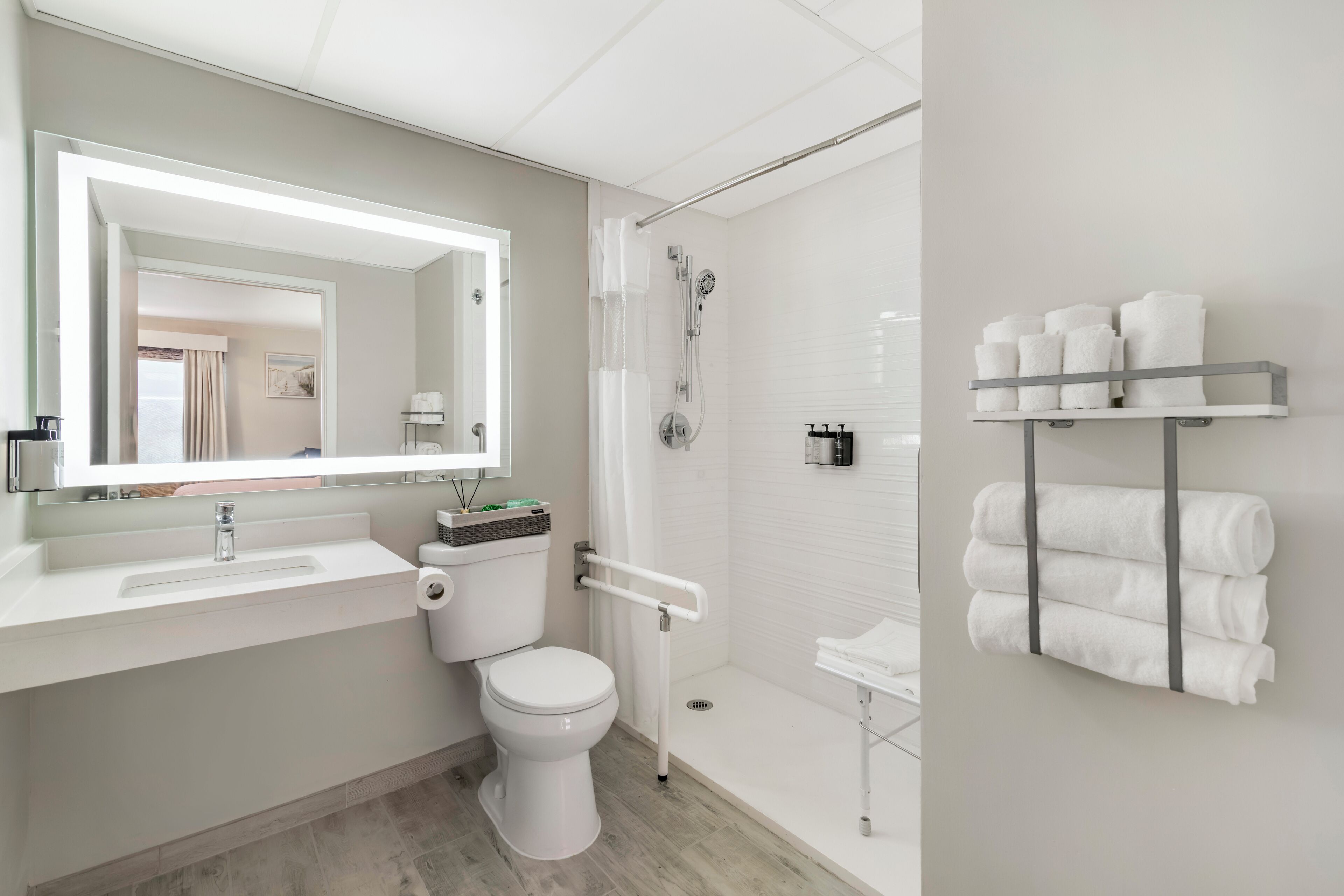 A modern bathroom with a white sink, toilet, and shower. There is a towel rack with towels on the wall.