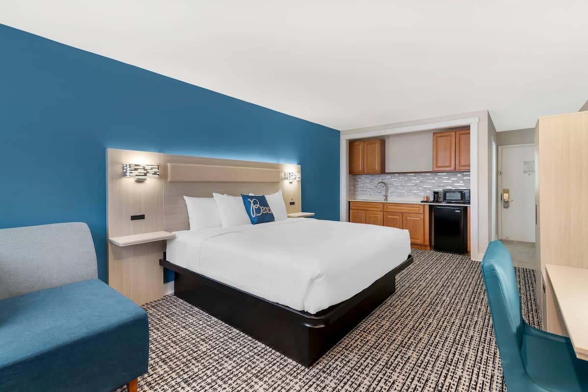 A hotel room with a bed, a desk, a chair, a kitchenette, and a bathroom.
