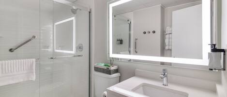 Un baño moderno con cabina de ducha de vidrio, un lavamanos blanco y un espejo grande.