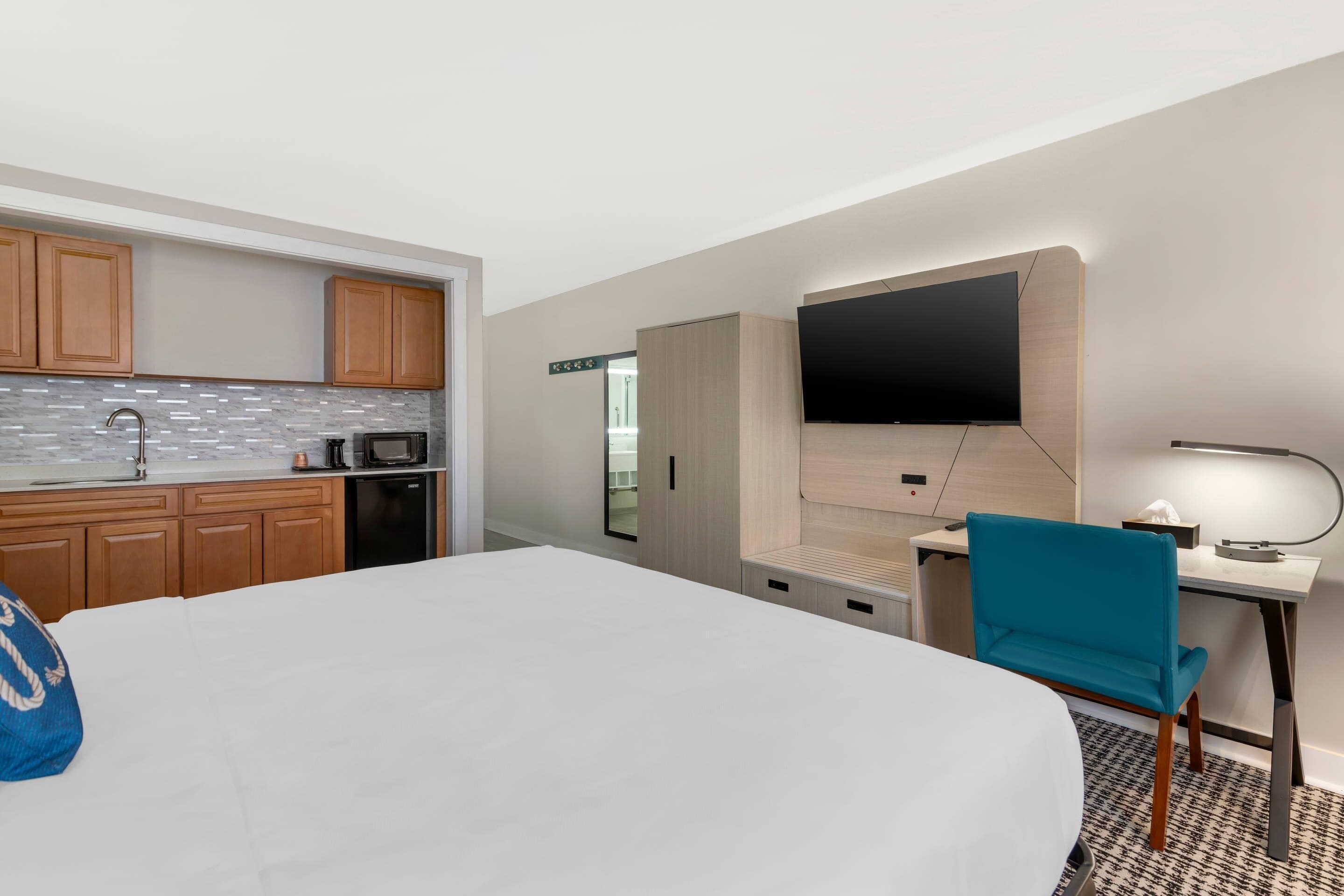 A hotel room with a bed, a desk, a chair, a TV, a microwave, and a small kitchenette.