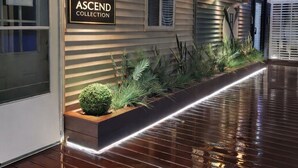 A hallway with a sign reading 'ASCEND COLLECTION,' a wooden planter with plants, and a reflective floor. - Heritage House Inn on Cape Cod, an Ascend Collection Hotel (Hyannis)