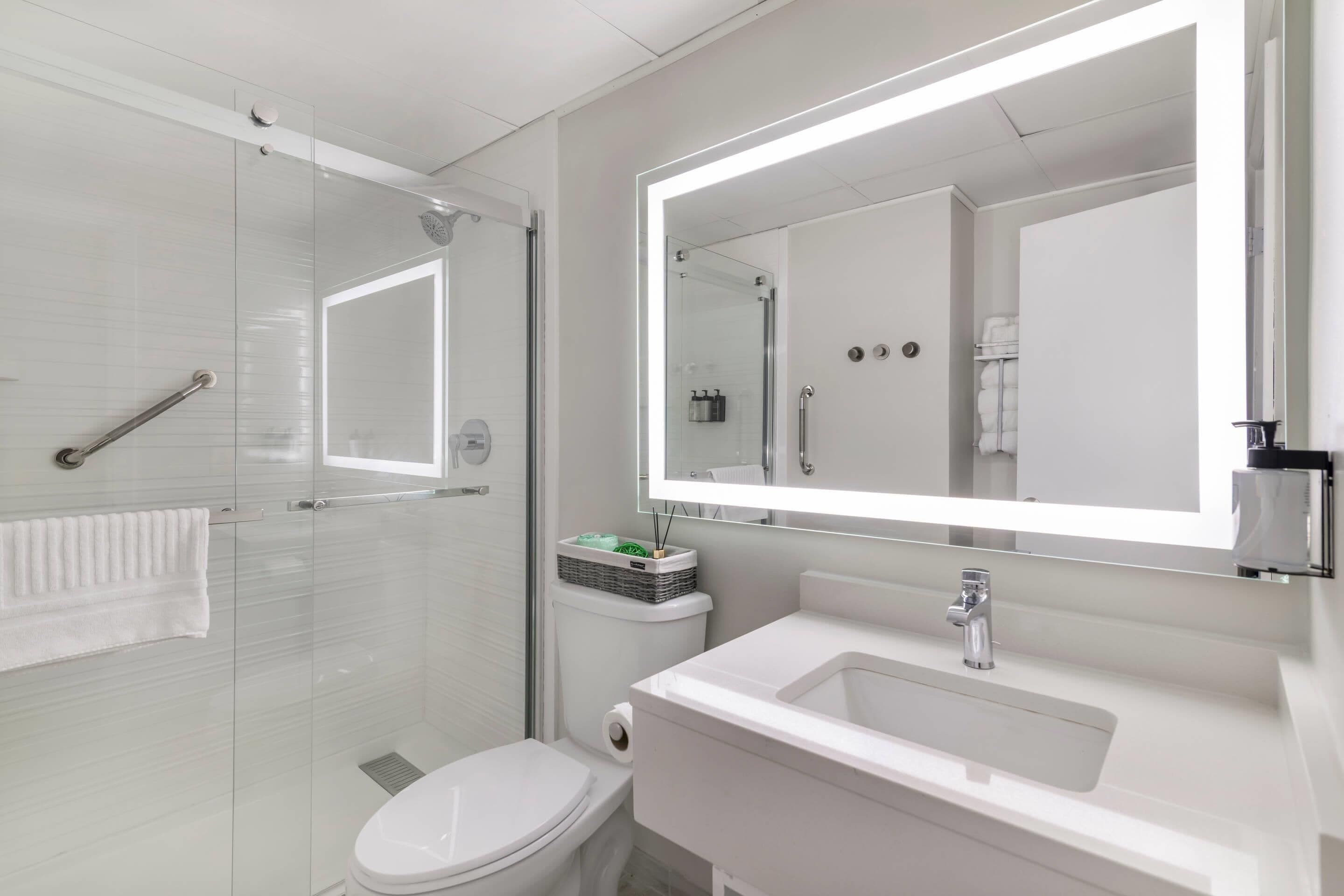 A modern bathroom with a glass shower enclosure, a white toilet, a sink with a mirror, and a towel rack.
