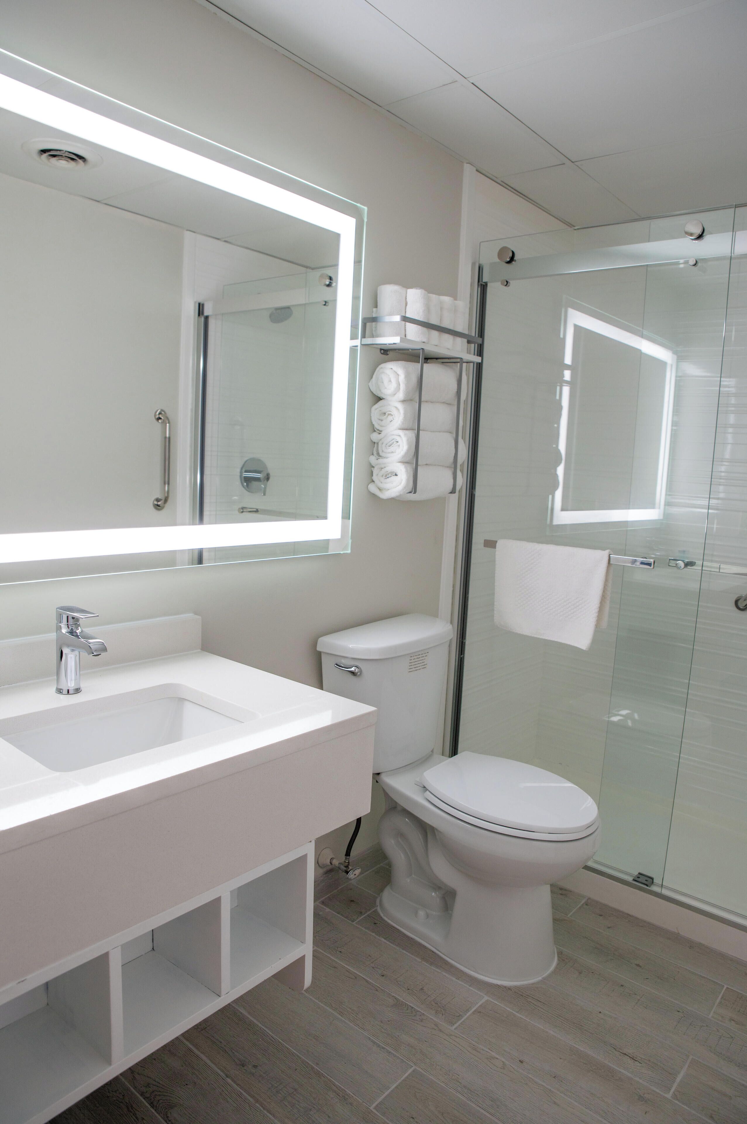 A modern bathroom with a white sink, mirror, toilet, and glass shower enclosure.