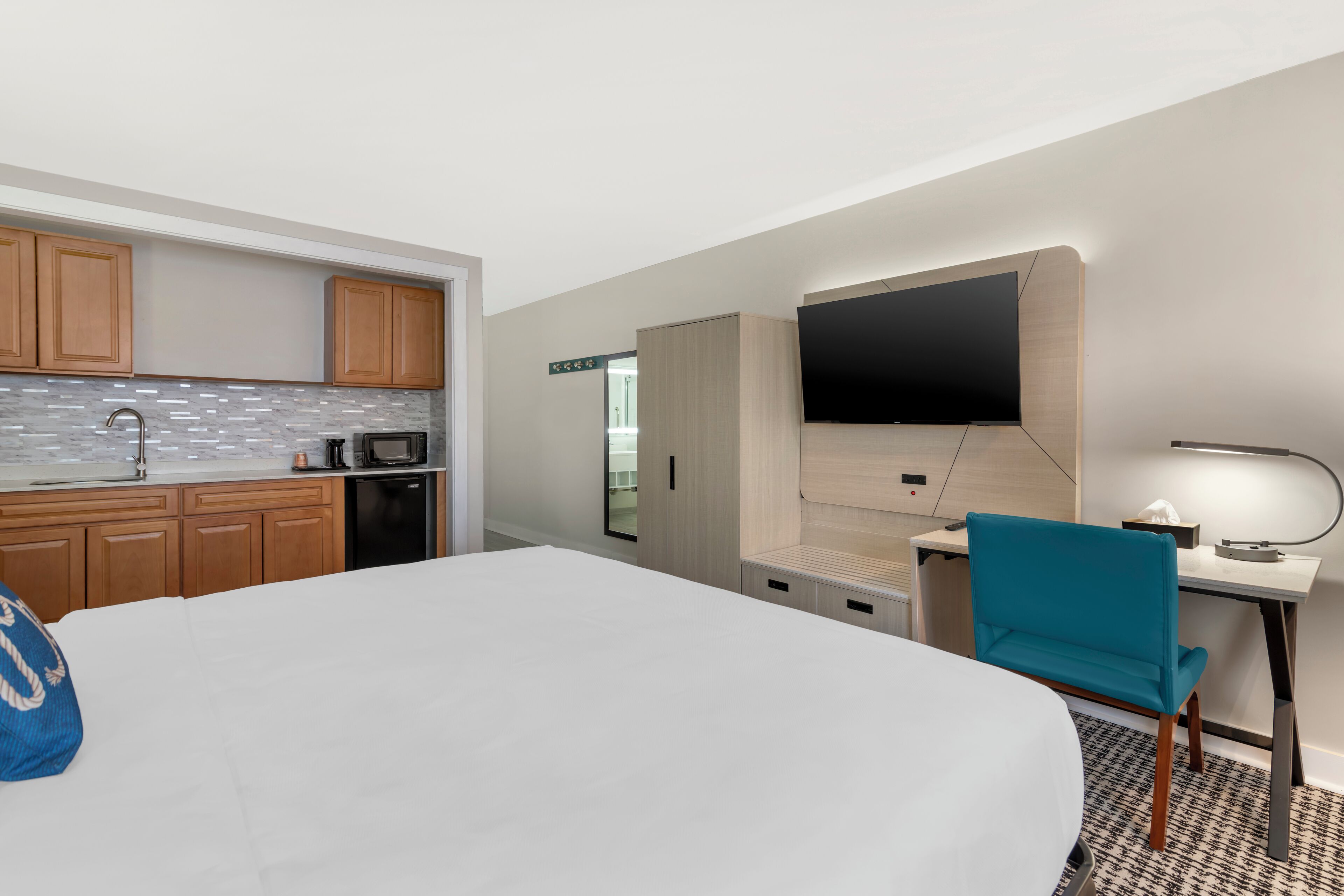 Habitación de hotel con cama, escritorio, silla, televisión, microondas y armarios de madera.