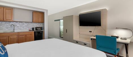 Habitación de hotel con cama, escritorio, silla, televisión, microondas y armarios de madera.