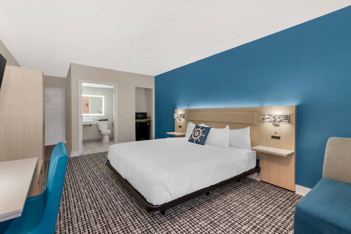 A hotel room with a large bed, a desk, a chair, a nightstand, and a bathroom visible through an open door.