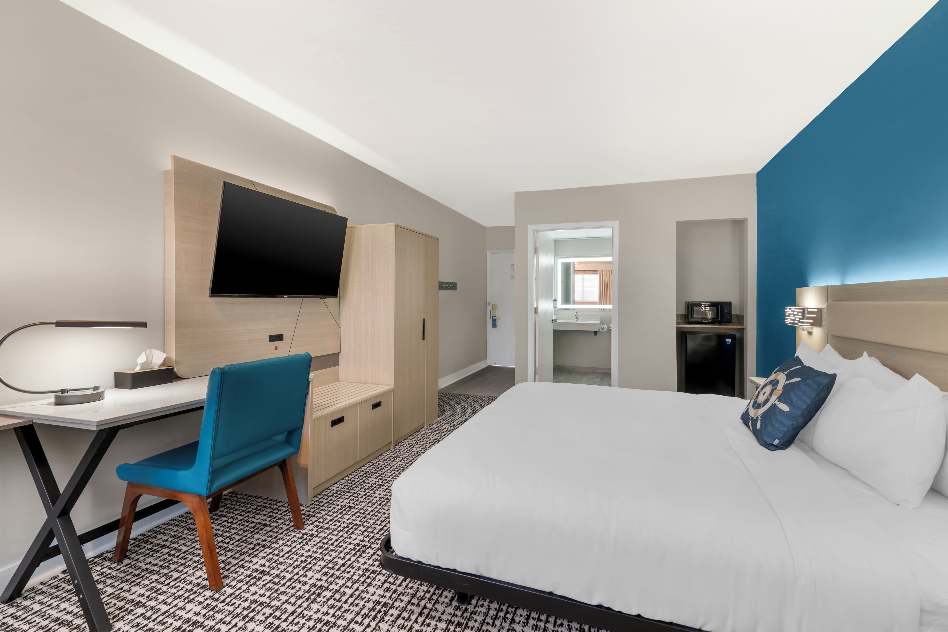 Una habitación de hotel con una cama, un escritorio, una silla, un televisor y un armario.
