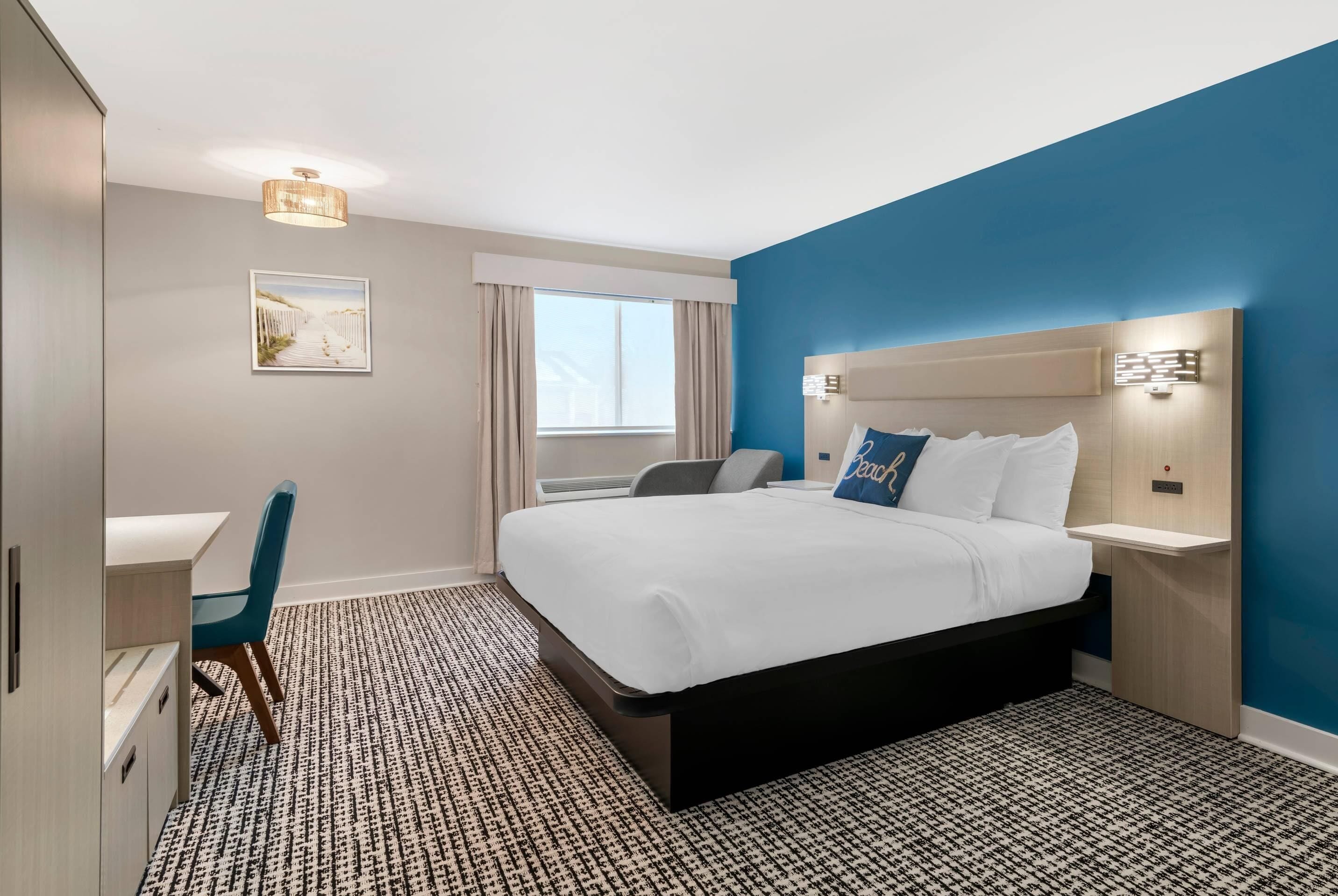 A hotel room with a bed, bedside table, chair, desk, and a window with curtains.