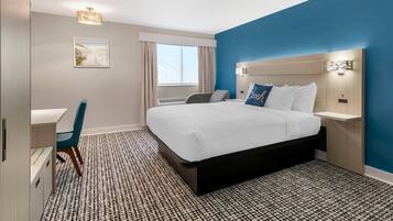 A hotel room with a bed, bedside table, chair, desk, and a window with curtains.