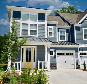 Une maison à deux étages avec un porche à l’avant, un garage et une pelouse bien entretenue.