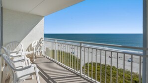 A balcony with white chairs, a view of the beach, and a clear sky. - Sanabel 503, 2BR 2BA Oceanfront Condo with Indoor Pool (North Myrtle Beach)