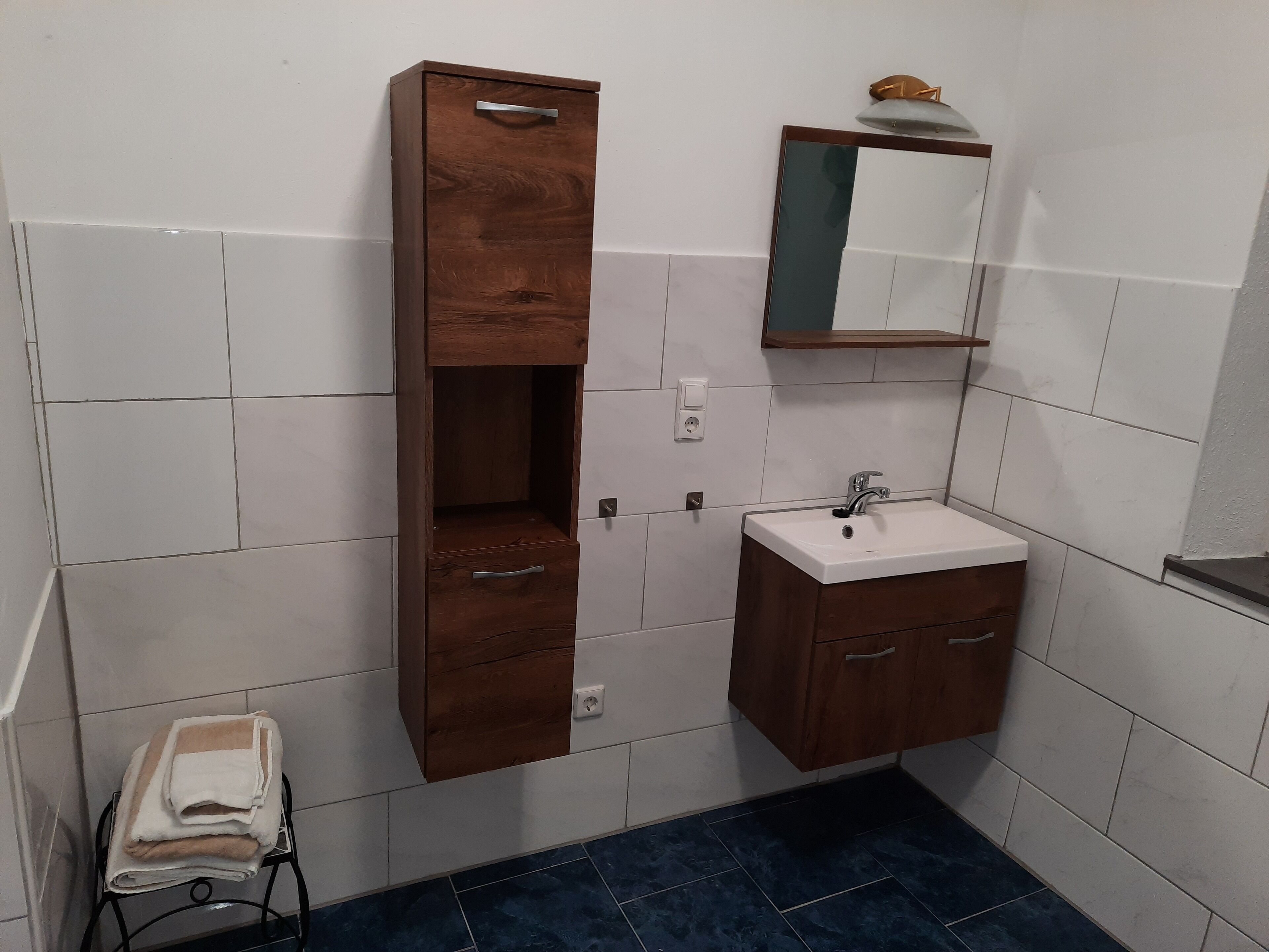 Ein Badezimmer mit weißen Fliesen, einem Holzkorpus mit Schubladen, einem Waschbecken und einem Spiegel.