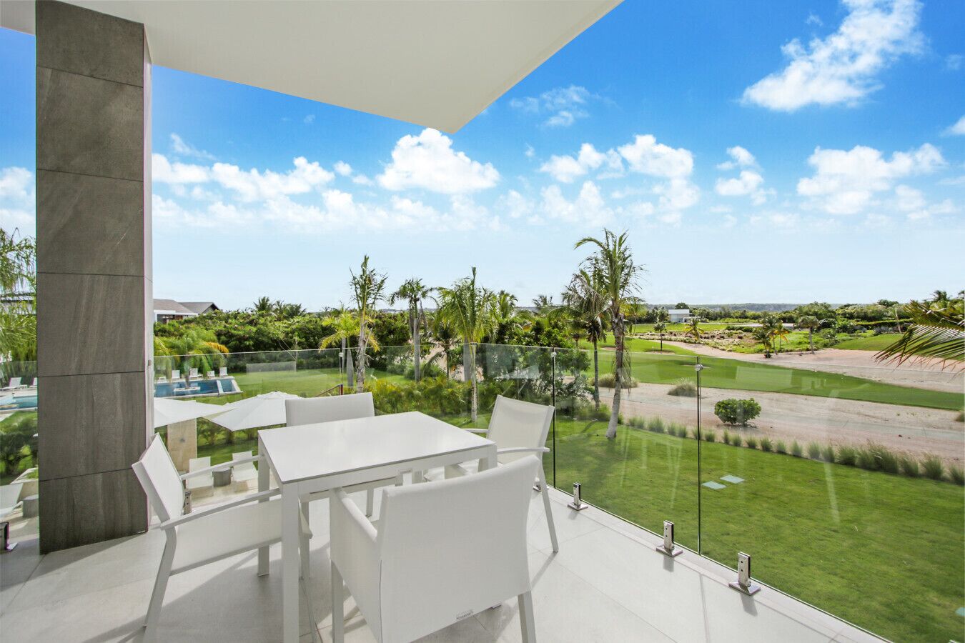 Um pátio moderno ao ar livre, com mesa e cadeiras brancas, com vista para um gramado bem cuidado e um campo de golfe.