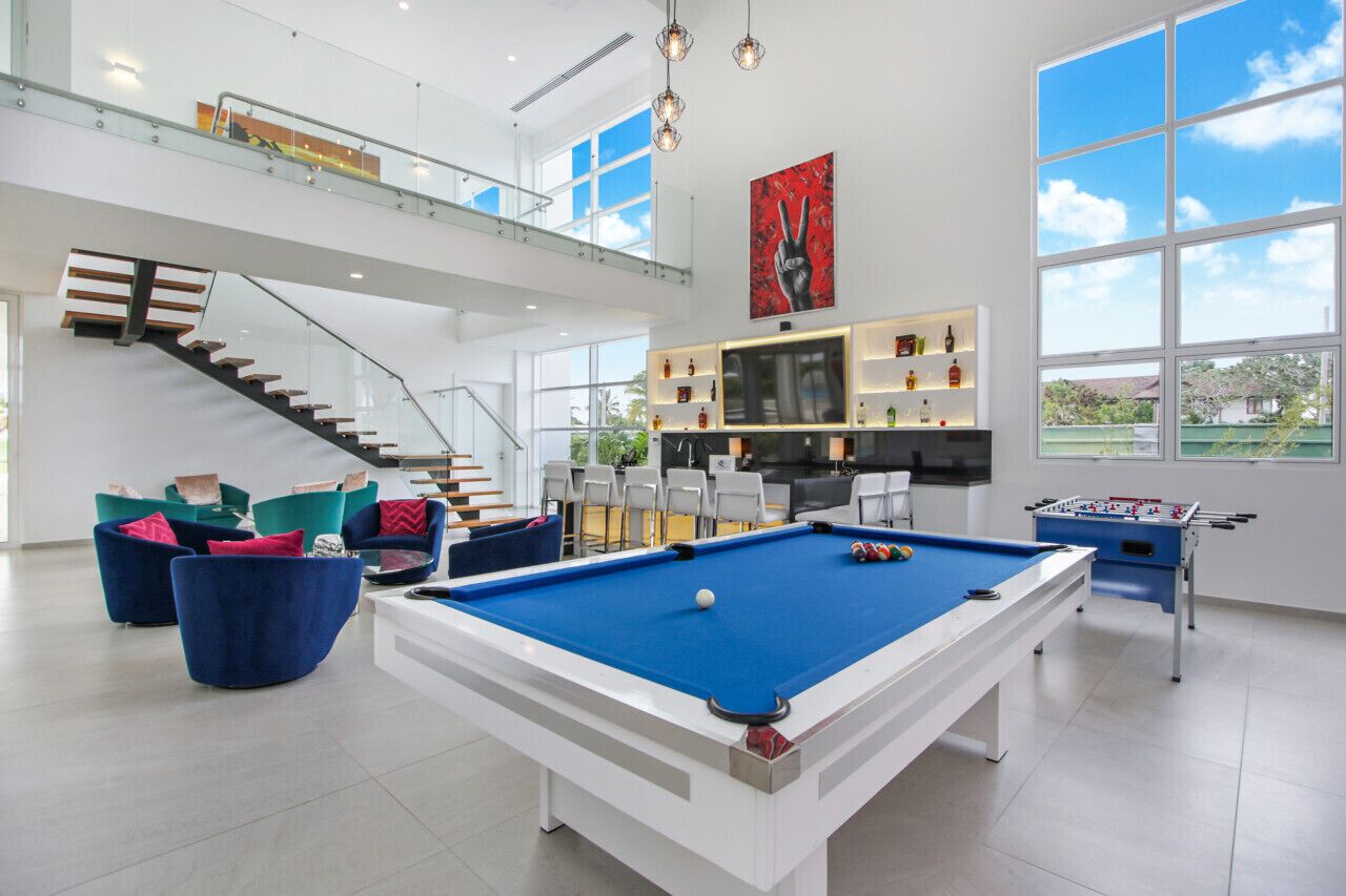 A spacious indoor area with a pool table, foosball table, and comfortable seating. A staircase leads to an upper level.