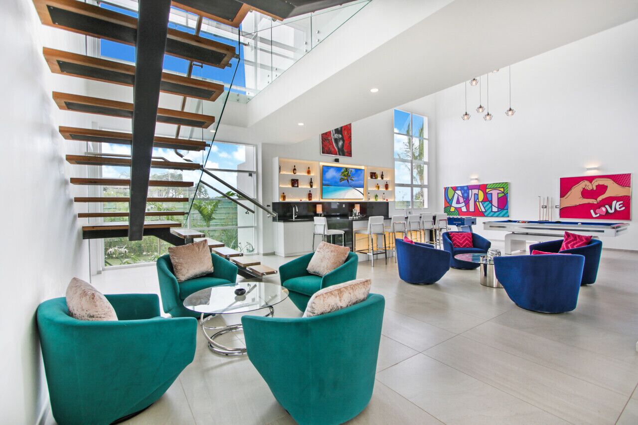 A spacious living area with teal sofas, a glass coffee table, and a kitchen in the background.