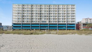 A large, multi-story hotel with a blue and white facade, located on a sandy beach. - Sanabel 609: Oceanfront 2BR/2BA- Indoor Pool (North Myrtle Beach)