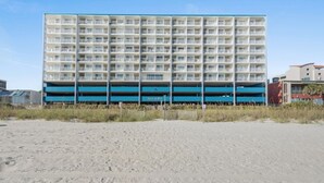 A multi-story hotel with a blue and white facade, located on a sandy beach.