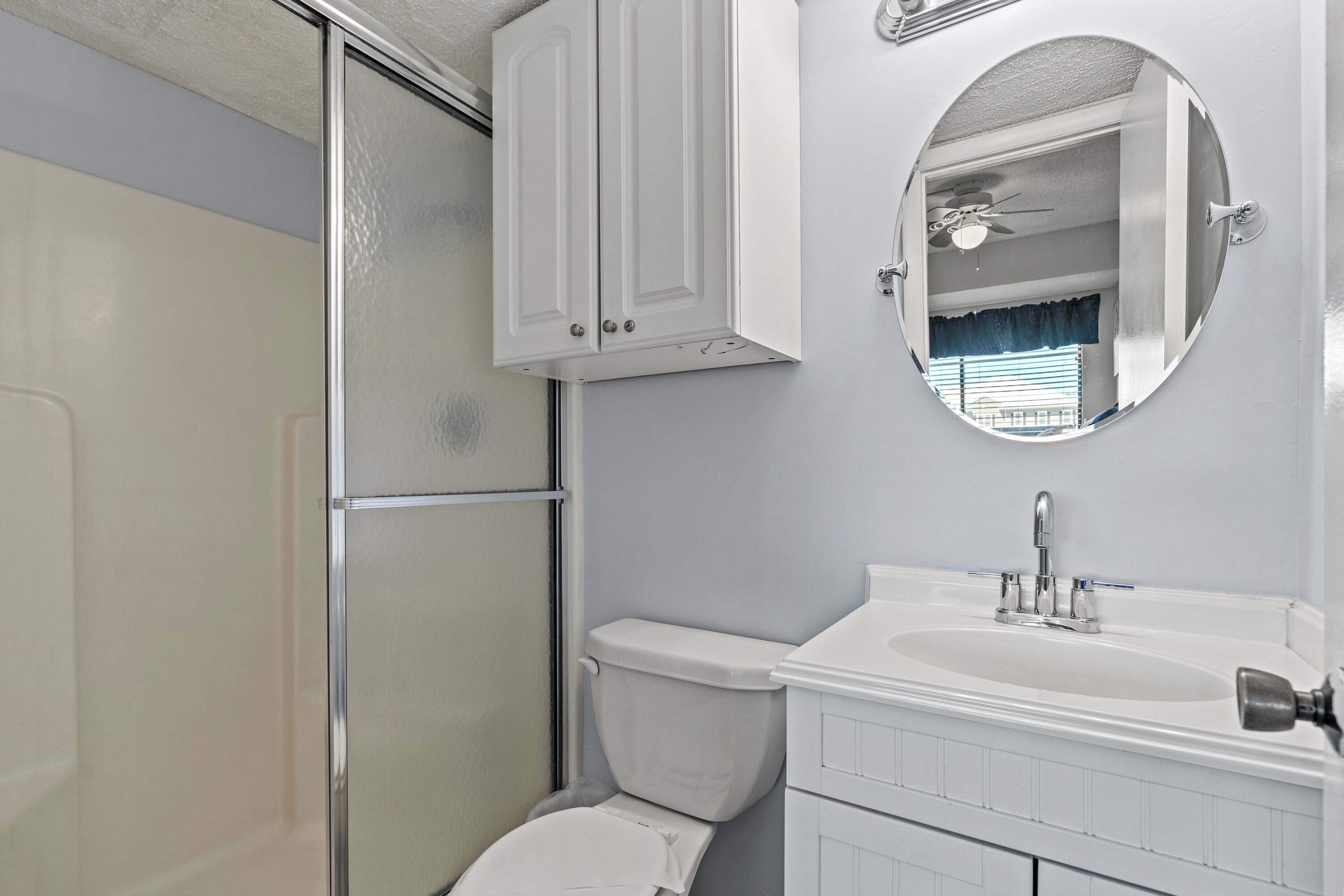 A bathroom with a shower, toilet, sink, and mirror.