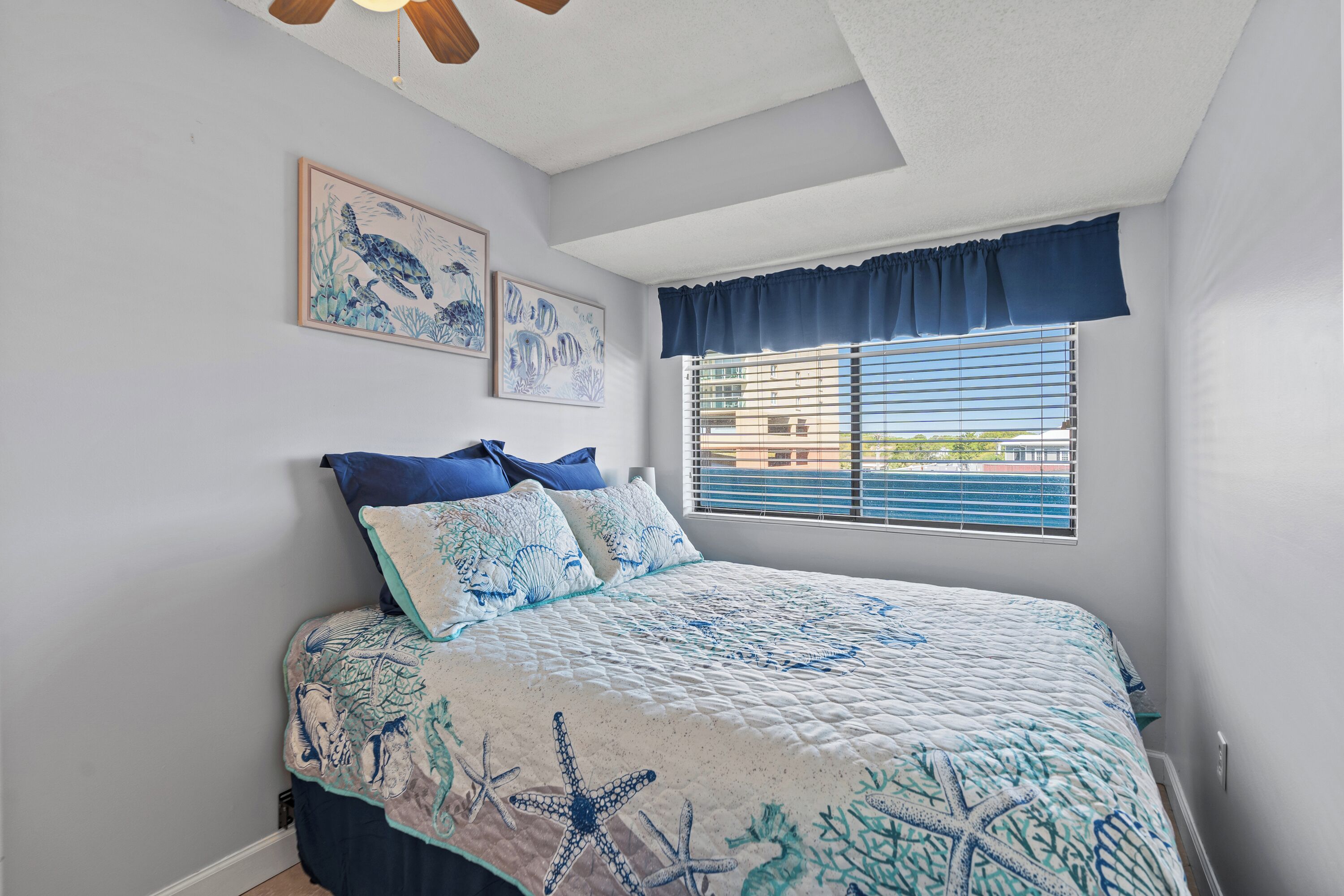 A bedroom with a bed, a window with blinds, and two wall-mounted pictures.