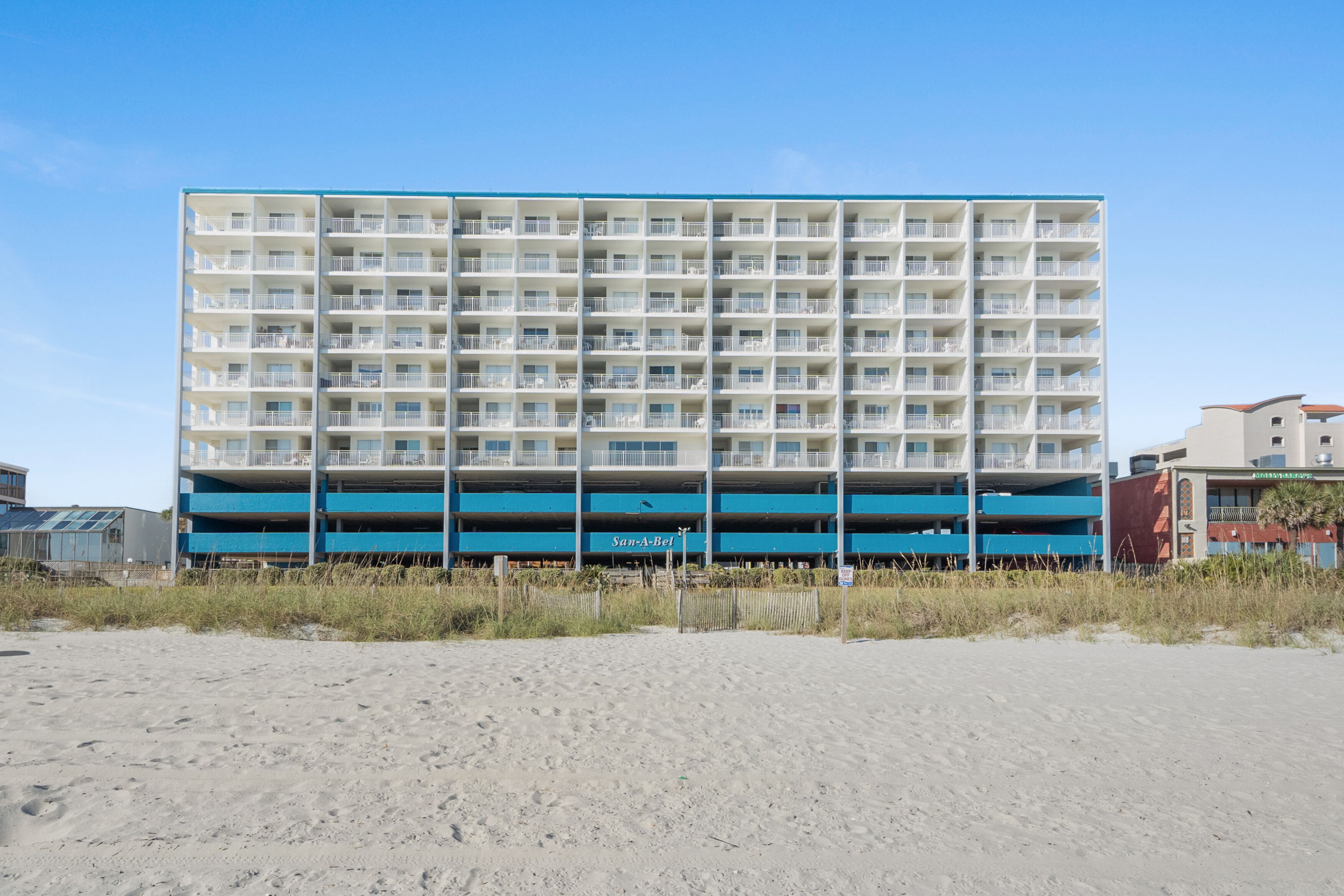 Un hôtel à plusieurs étages, à la façade bleue et blanche, situé sur une plage de sable.