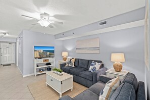 Sala de estar com sofá cinza, móvel de entretenimento branco e ventilador de teto.
