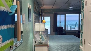 A bedroom with a bed, a nightstand, a lamp, a window with a view of the sea, and a door leading to a balcony. - Let it BEach - Beach Property (Panama City Beach)