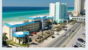 A hotel with a blue roof, located near a beach and a road with cars. - Let it BEach - Beach Property (Panama City Beach)
