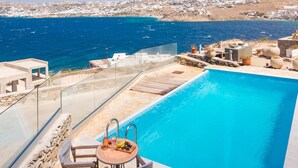 Zona de piscina con vista al mar y un pueblo lejano.