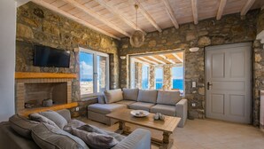 Una sala de estar acogedora con paredes de piedra, una chimenea, un sofá grande y un televisor.