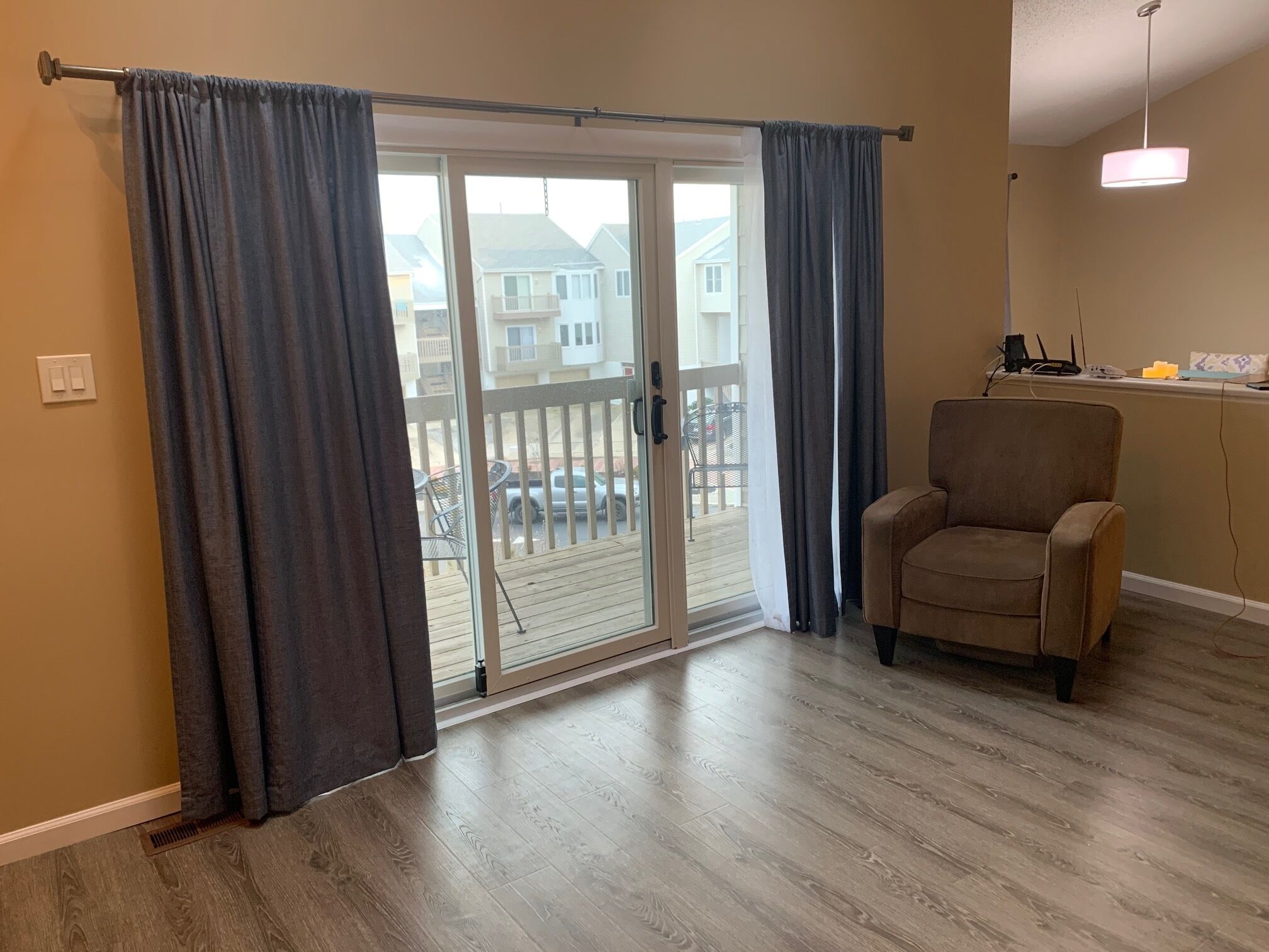 A room with a sliding glass door leading to a balcony, a brown armchair, and a ceiling light fixture.