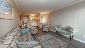 A living room with a sofa, two armchairs, a rug, and a kitchen in the background.