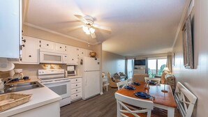 A compact kitchen with white cabinets, a microwave, a stove, and a refrigerator. There is a dining area with a wooden table and white chairs.