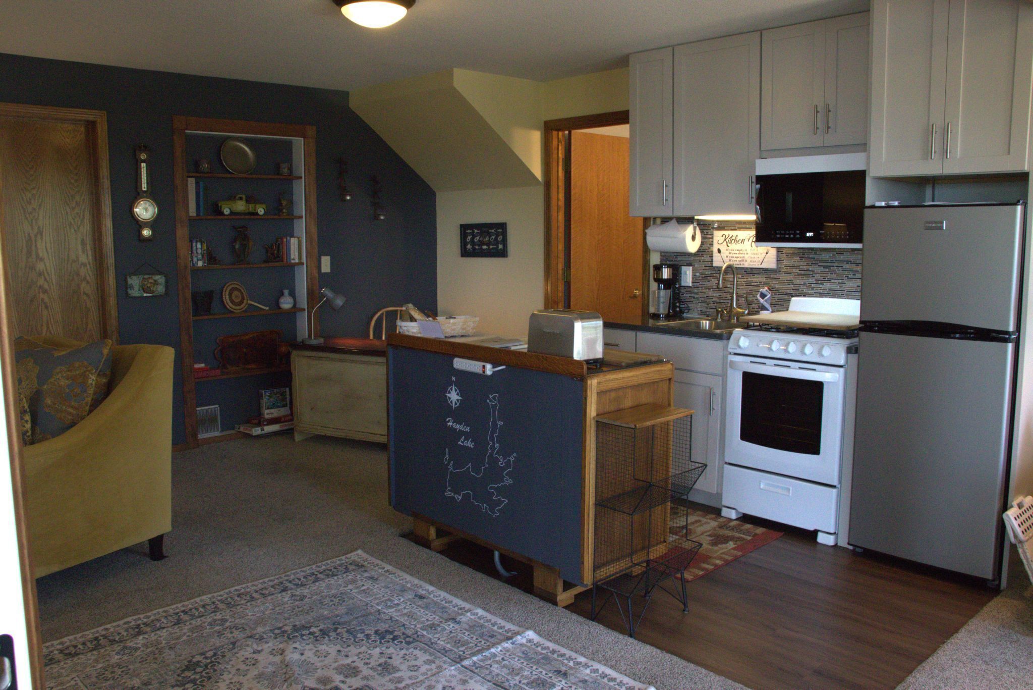 A kitchen with a refrigerator, stove, microwave, and a chalkboard with a map.