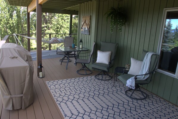 A covered outdoor patio with a table, chairs, a grill, and a patterned rug.