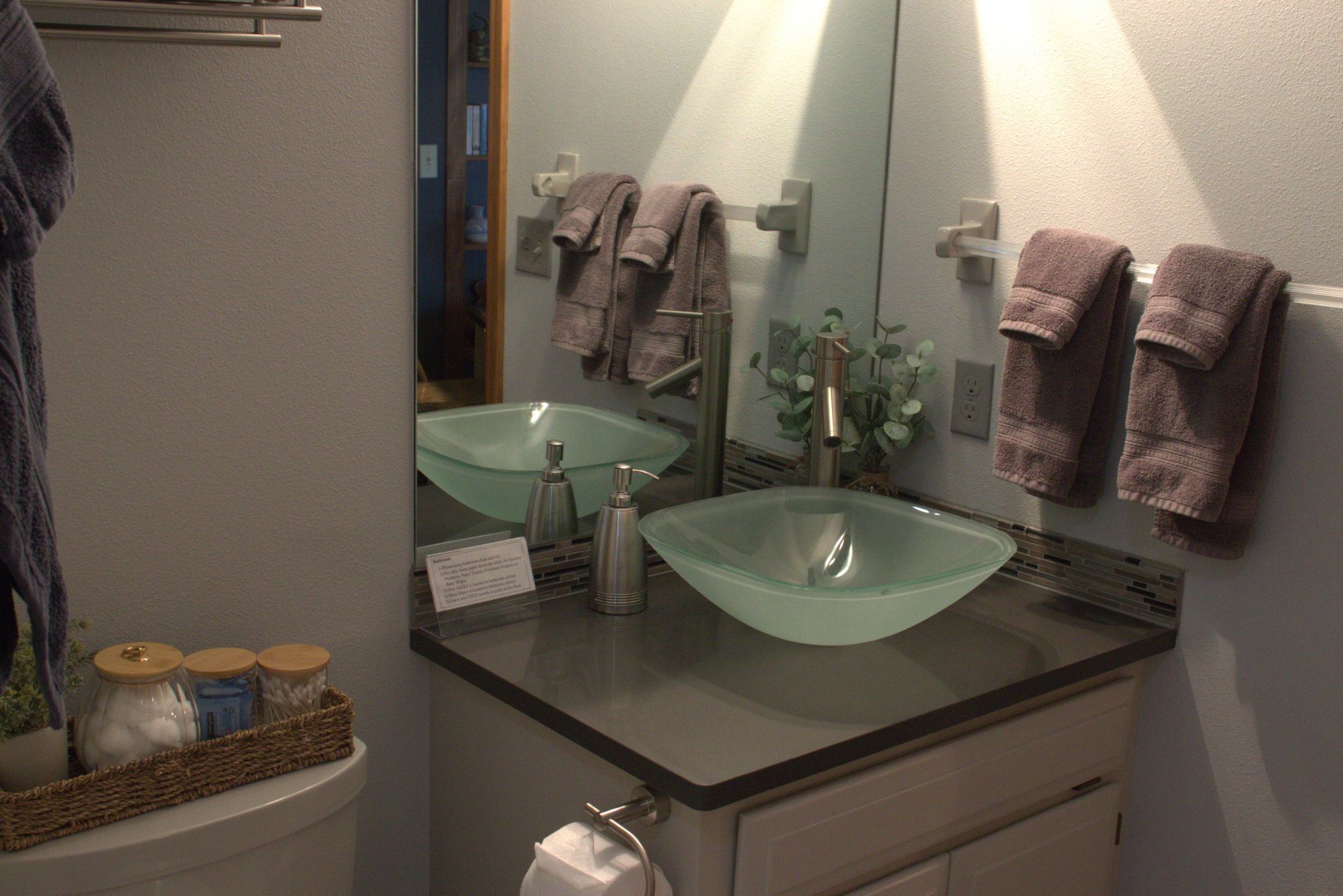 A bathroom with a glass sink, a mirror, and towels on a rack.