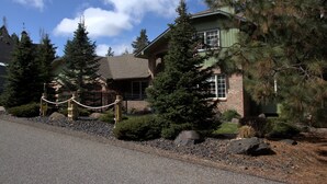A two-story house with a brick facade, large windows, and a well-maintained front yard with pine trees and shrubs. - Hayden Lake Retreat • Lake Views • Private Deck • Near Coeur d'Alene (Coeur d'Alene)