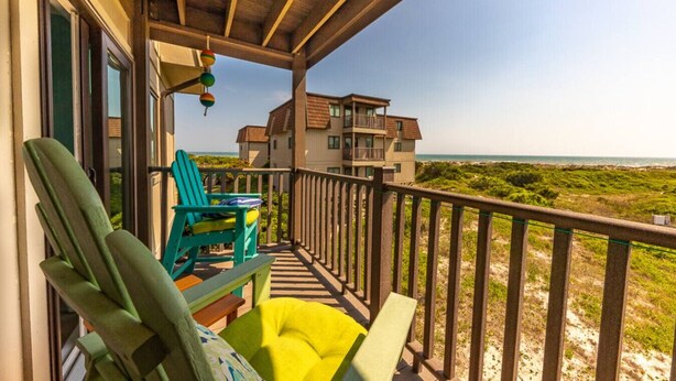 A balcony with a view of the beach, a wooden ceiling, and a building in the background. - Sea Dreams: Affordable Family Friendly: Ocean Views • Pool • Linens & Amenities (Atlantic Beach)