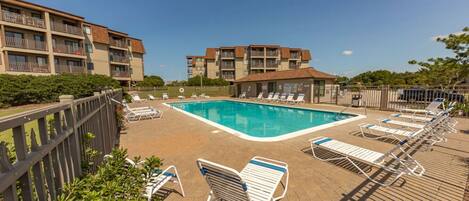 A pool area with lounge chairs and a clear blue pool surrounded by a wooden deck.