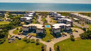 An aerial view of a coastal residential area with multiple apartment buildings, a swimming pool, and a beach in the background. - Sea Dreams: Affordable Family Friendly: Ocean Views • Pool • Linens & Amenities (Atlantic Beach)