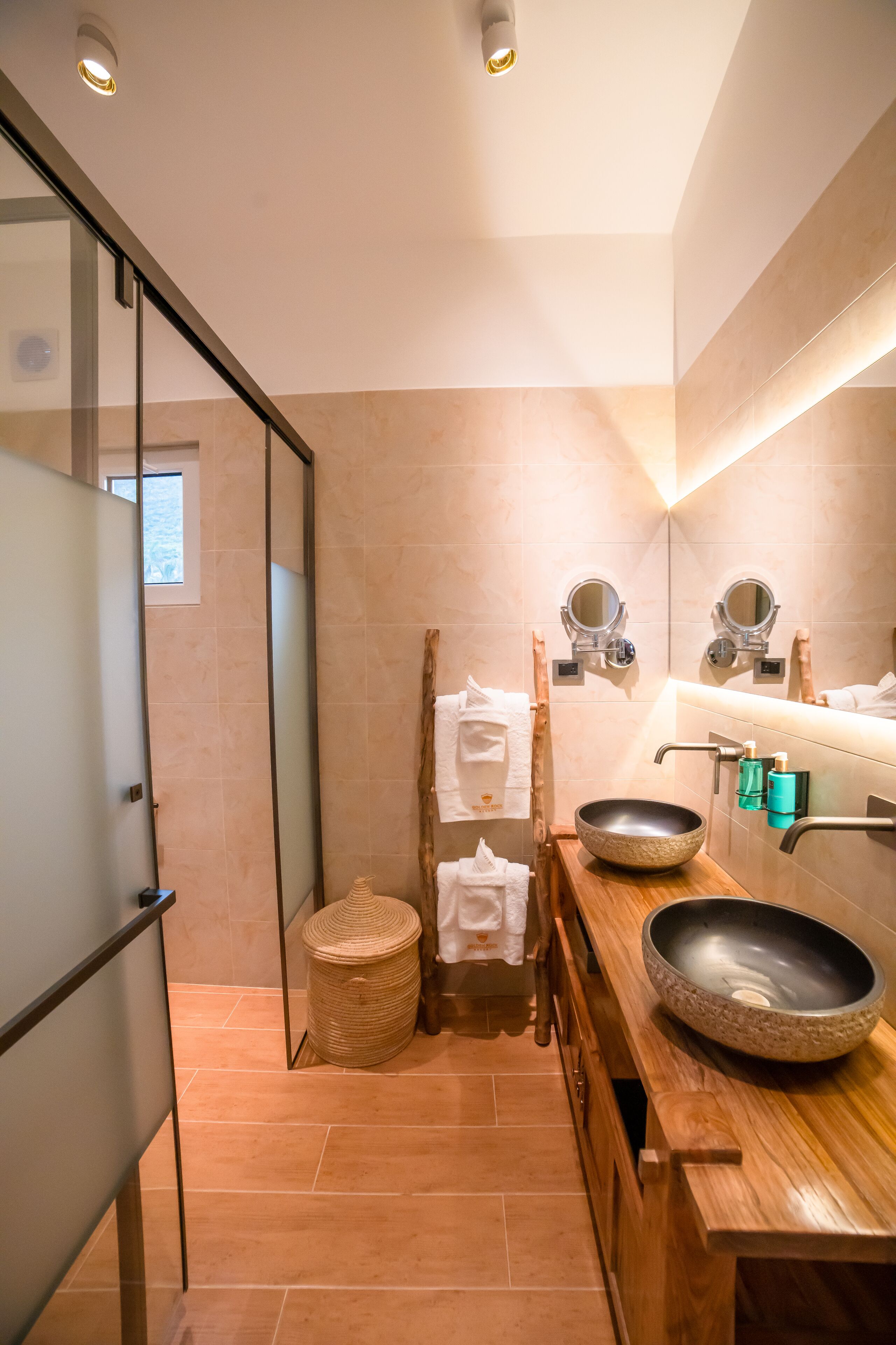 A modern bathroom with a glass shower enclosure, a wooden vanity with a large bowl sink, and a mirror above the sink.